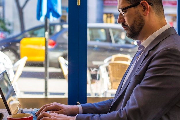A person working on a laptop at a coffee shop, with a financial graph visible in the background on the laptop screen. The image represents the gig economy worker juggling income and retirement planning.