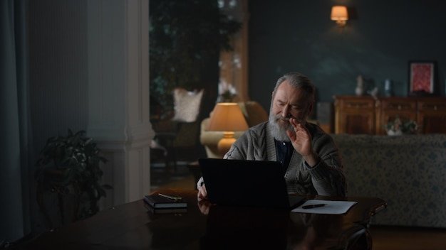 A person looking stressed while paying bills online using a laptop. The scene is set in a dimly lit room to convey the stress and anxiety associated with financial obligations.