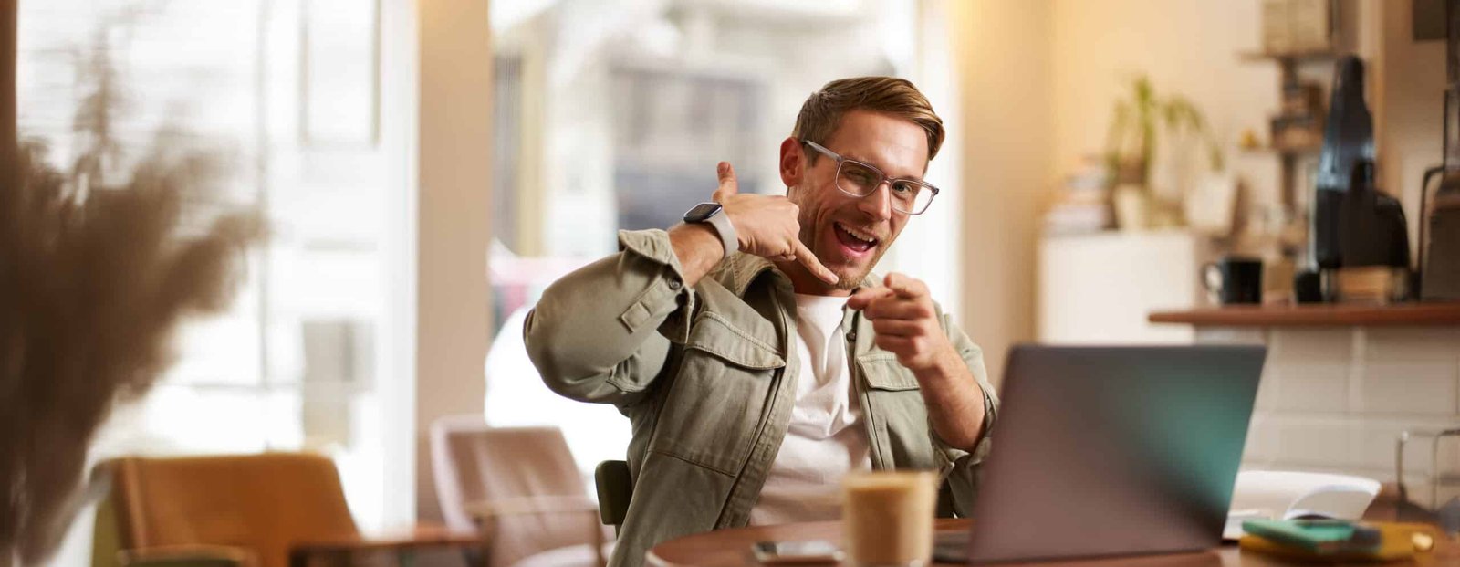 A person happily working on a laptop at a coffee shop, with a focus on the screen showing freelance project listings. The background shows other people working and enjoying their coffee.